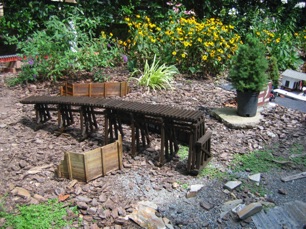 So, a trestle and bridge comination is in order. I've completed about 6 feet so far and today was the day to seal it. It's hot outside, but it was so much easier applying it there than down in my work room. Of course now I have some sealed mulch as well. Hidden by the trestle is my Garden Metals Model bridge. 