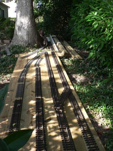 It will look something like this where I've just laid the track on the boards that will make up the base of the yard. You can see I don't have a lot of room to get around the tree. I'll be building a turntable that will go just to the left of the boards in the picture. And, not much room in the other direction. 