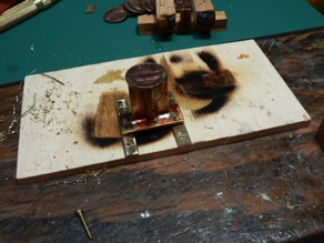 A penny is soldered to the top, and the legs are soldered in place. Next, I drill a hole for the brass rod and cut slots in the penny.